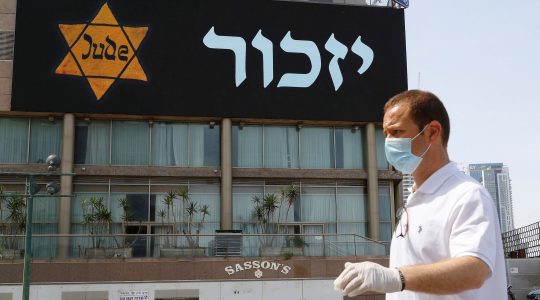 A man in a mask and protective gear stands near a banner depicting a Holocaust-era yellow Star of David in Tel Aviv on April 21, 2020. (Jack Guez/AFP via Getty Images)