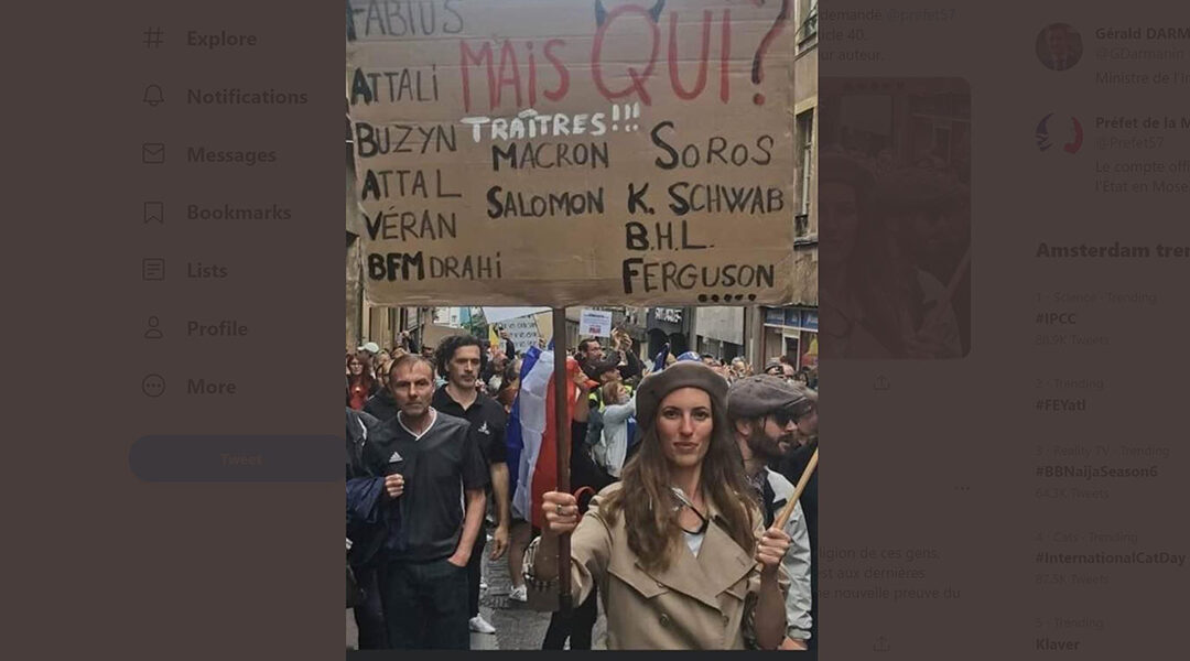 A woman holds up a placard denouncing President Emmanuel Macron and several prominent Jews denounced as traitors at a protest against COVID restrictions in Metz, France on Aug. 7, 2021. (Gérald Darmanin/Twitter)