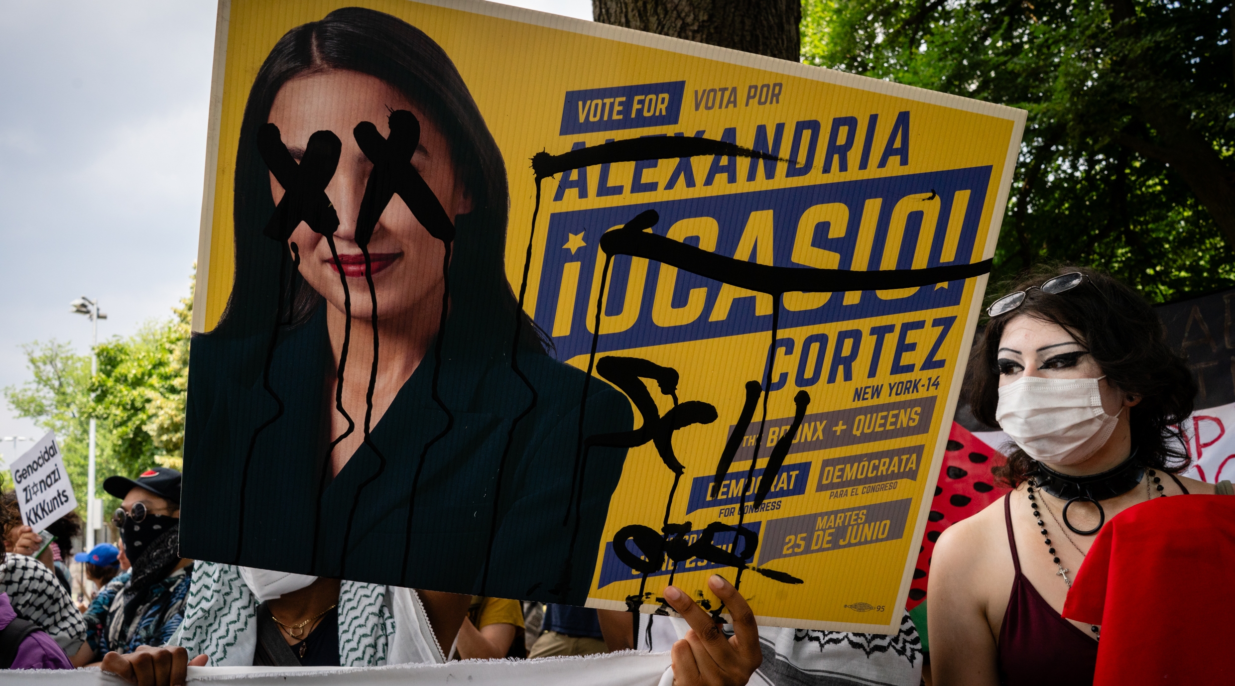 Anti-Israel protesters holding a defaced campaign sign for New York Rep. Alexandria Ocasio-Cortez outside a rally in the Bronx, June 22, 2024. (Luke Tress)