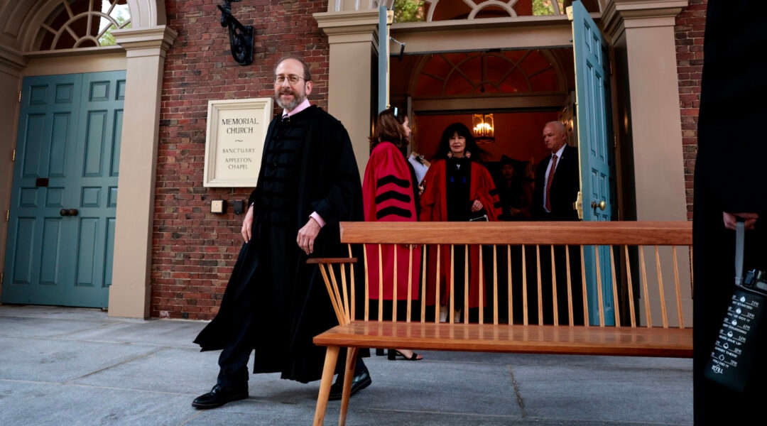 A university president in a gown walks out a door during commencement