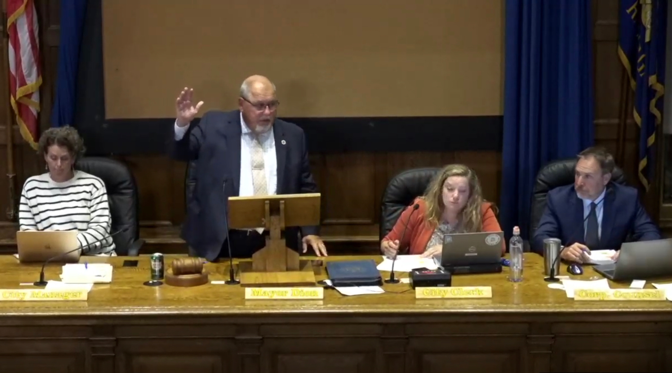 A mayor stands and raises his hand to vote during a city council meeting