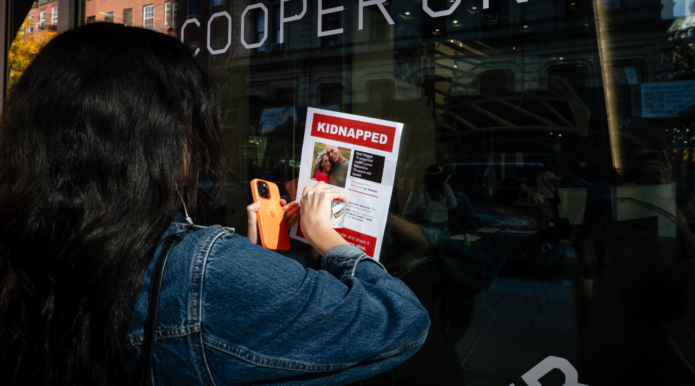 A woman puts a hostage poster on the entrance to Cooper Union college after Jewish students were harassed, Oct. 26, 2023. (Luke Tress)