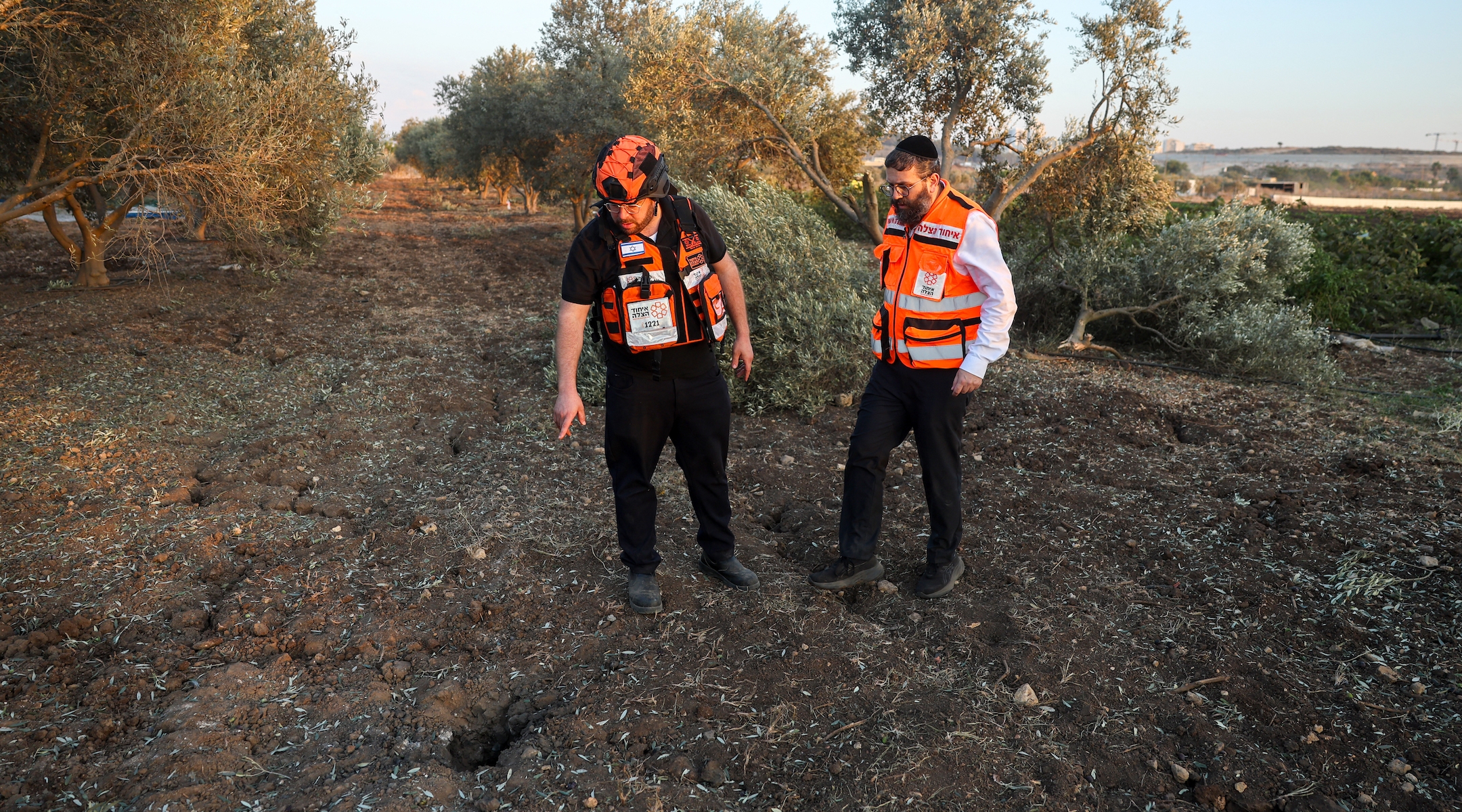 First responders stand next to a crater where a rocket fired from Lebanon hit an area in northern Israel's Haifa district on October 31, 2024 (Ahmad Gharabli/ AFP)