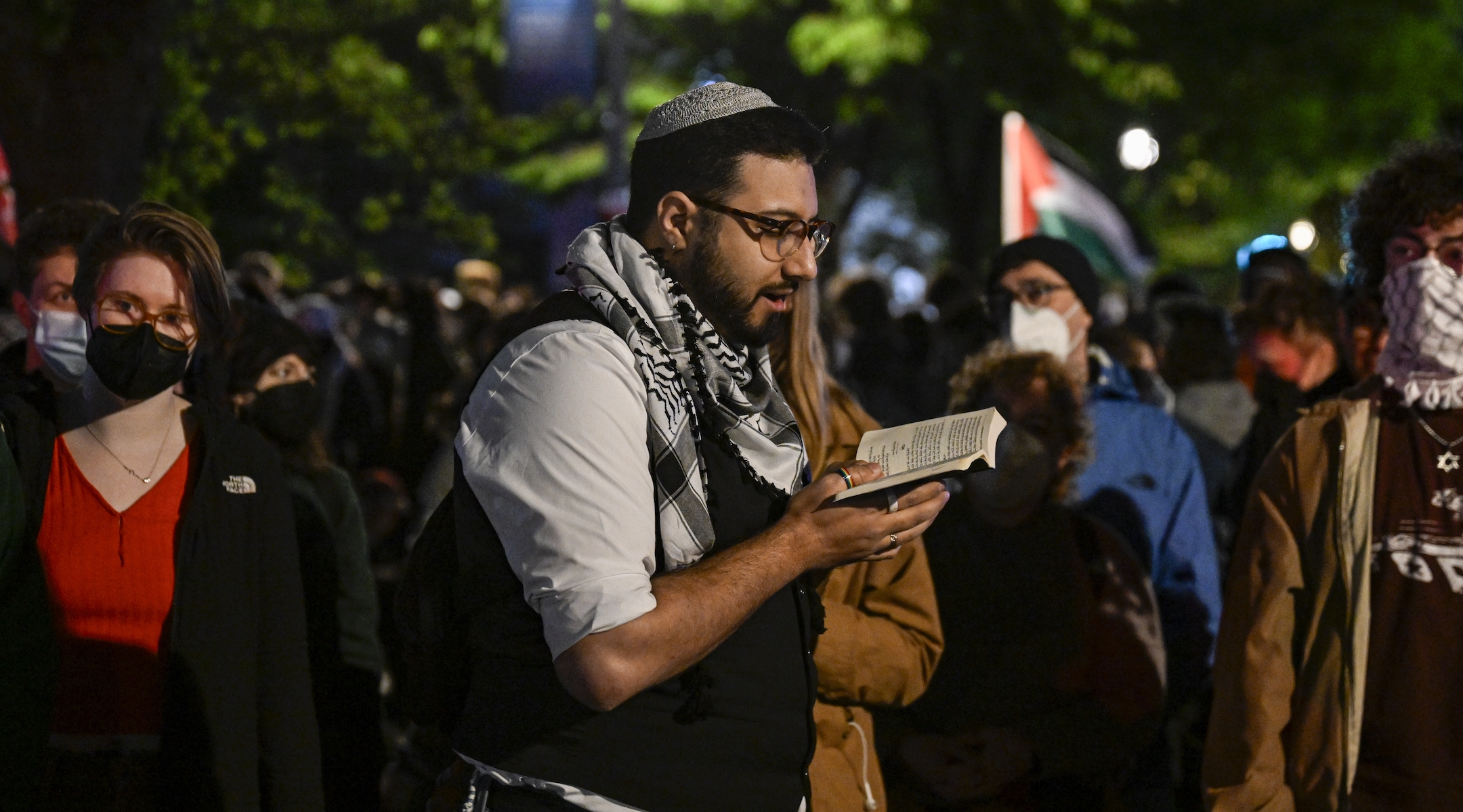 A Jewish student prays at night while wearing a keffiyeh and a yarmulke during a pro-Palestinian encampment protest