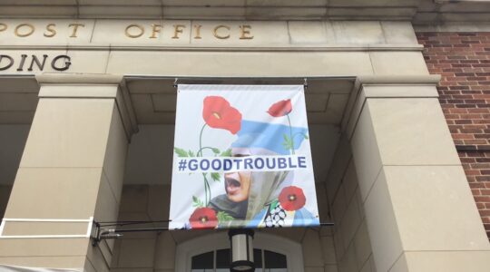 A banner depicting a student in a graduate gown and a keffiyeh with "#GOODTROUBLE" written across it