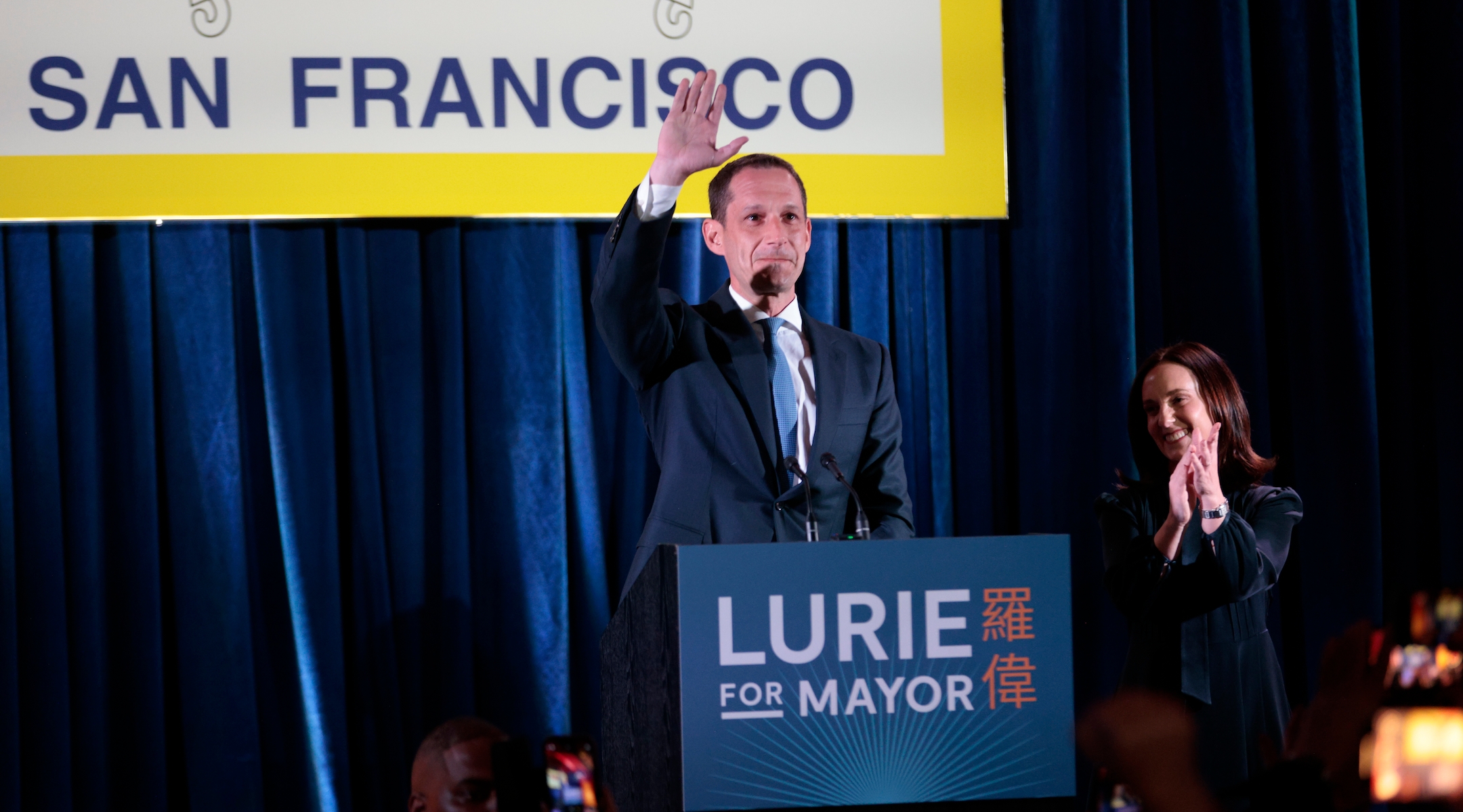 Mayoral candidate at a podium waving to supporters