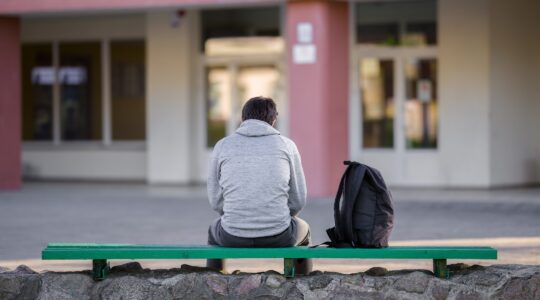 One young man sitting on bench at school yard.