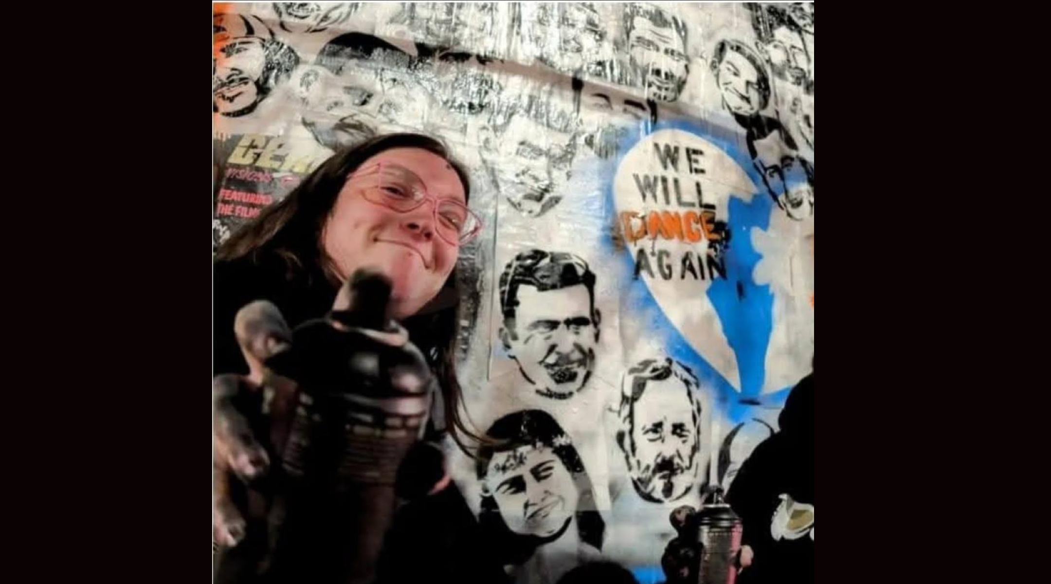 A street artist shows off a mural with the words "We Will Dance Again"