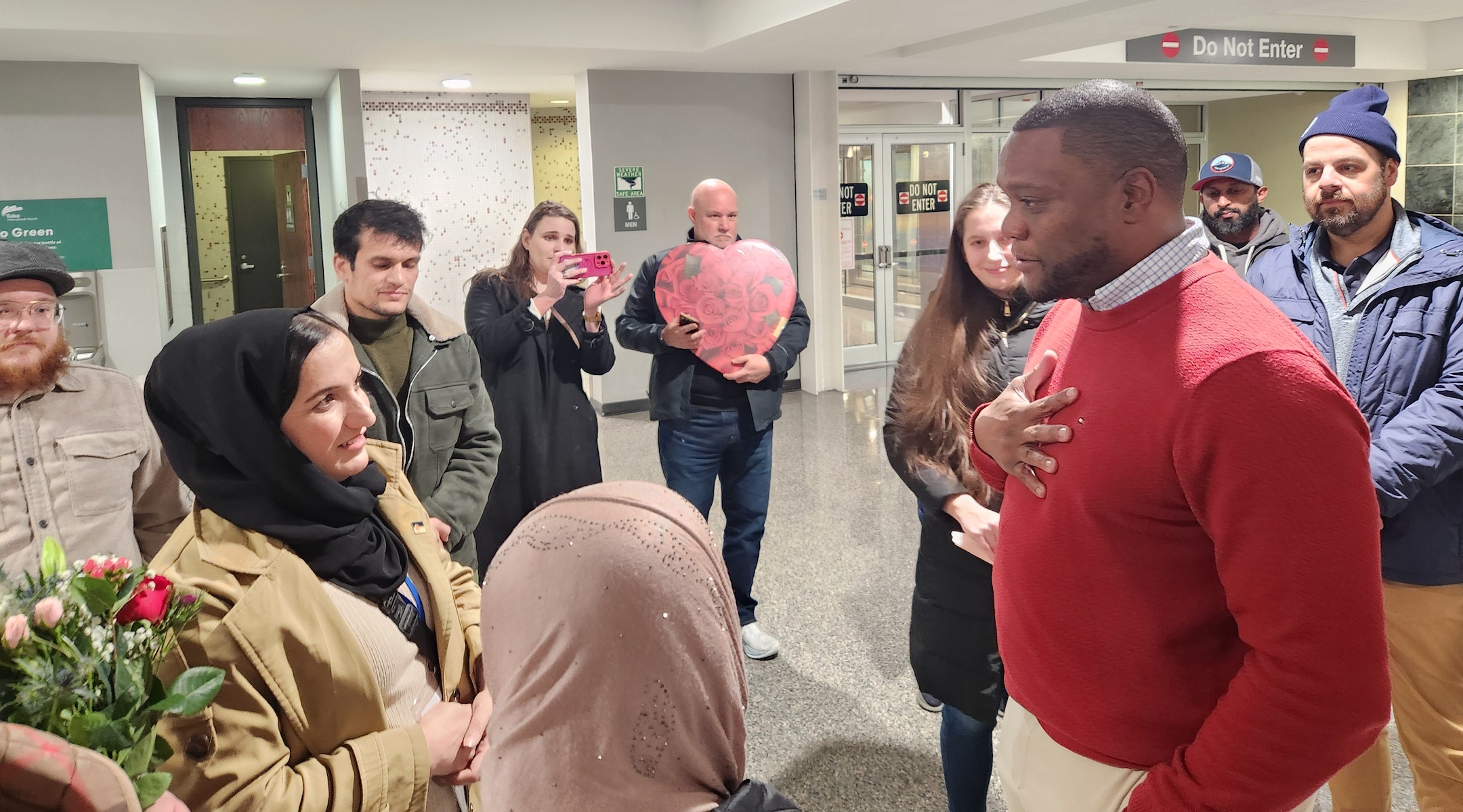 A refugee is welcomed to the United States in an airport with a large group of people