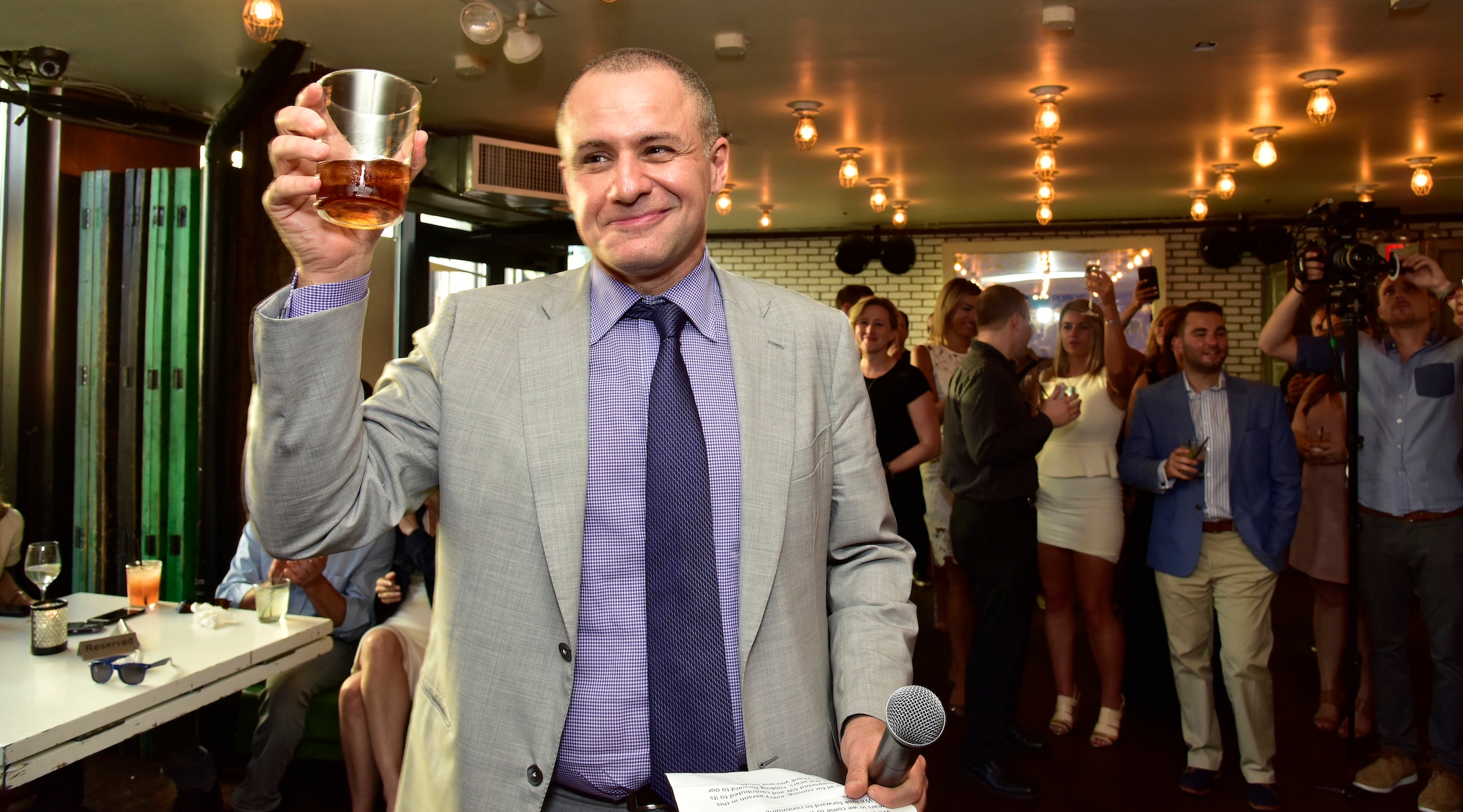 A man in a suit holds up a glass to toast